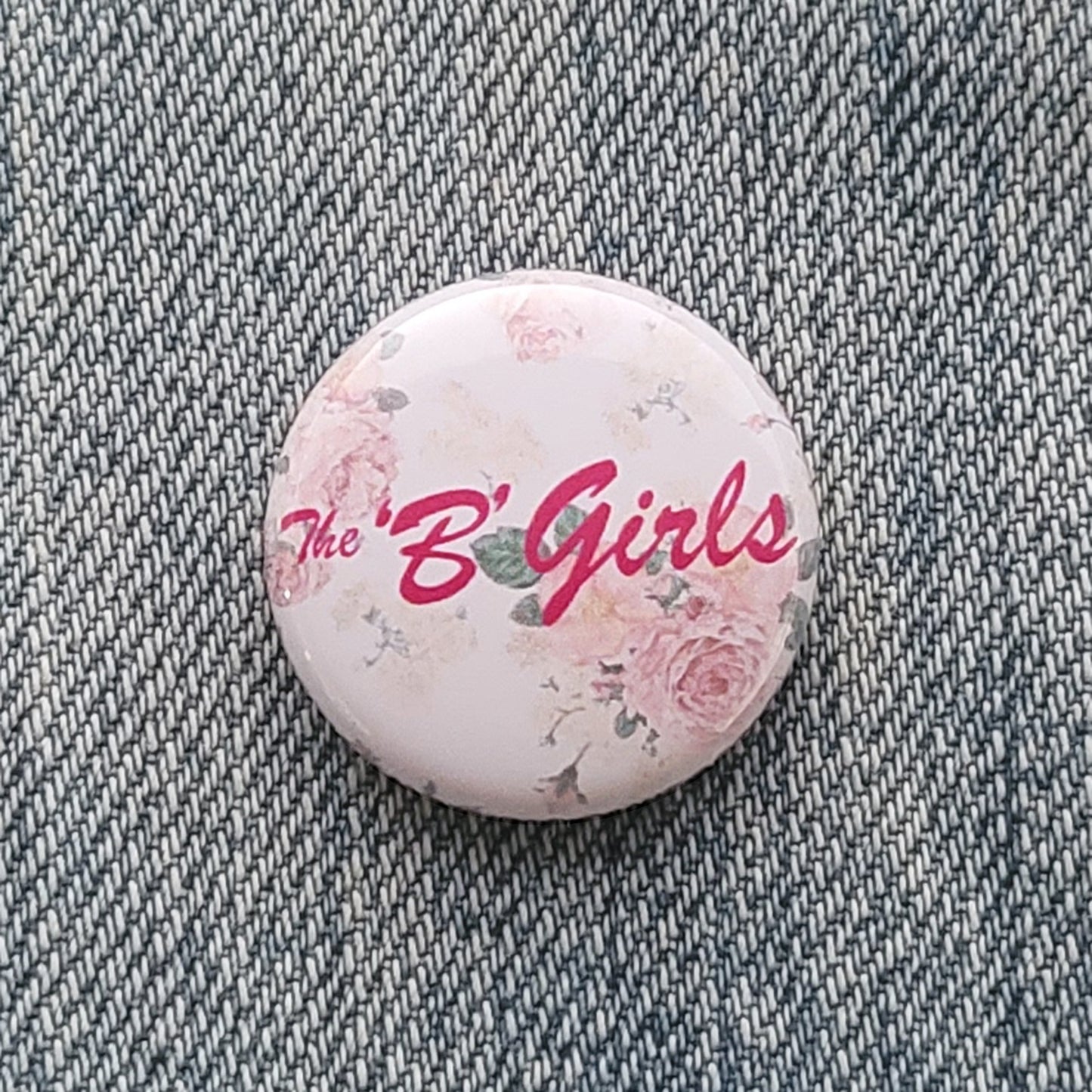 The 'B' Girls 1" pin with their pink logo over subtle pastel floral background